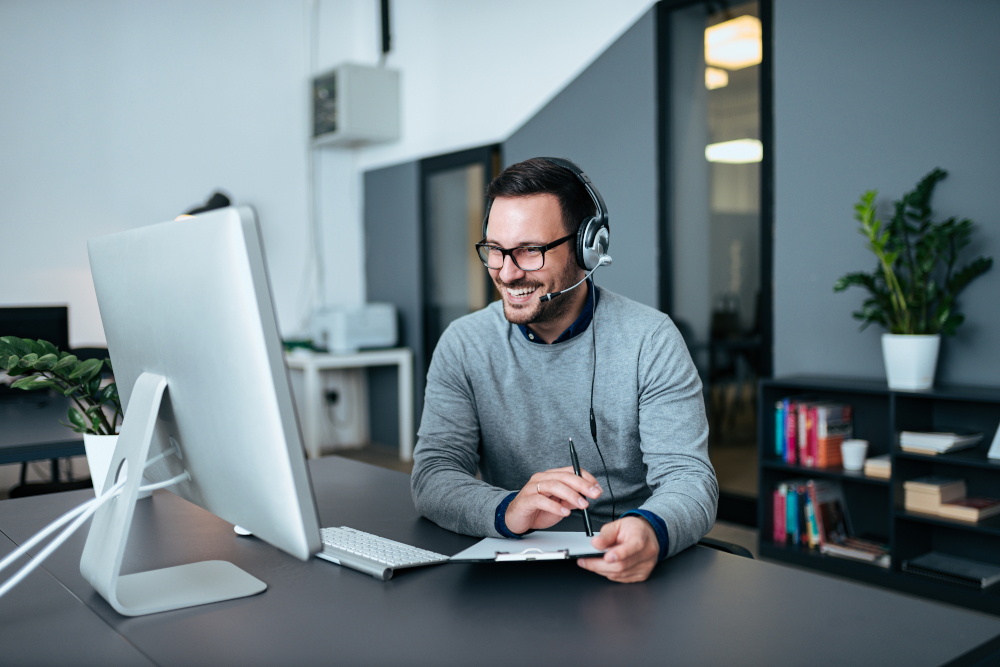 Freundlicher IT-Supportmitarbeiter mit Headset am Computer, Symbol für technische Beratung und Kundendienst.